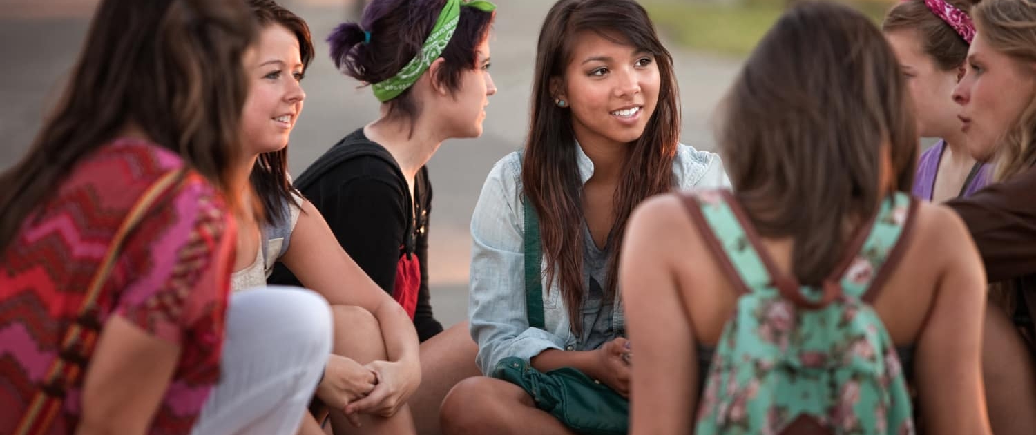 A group of teen girls sit talking with each other in a supportive manner